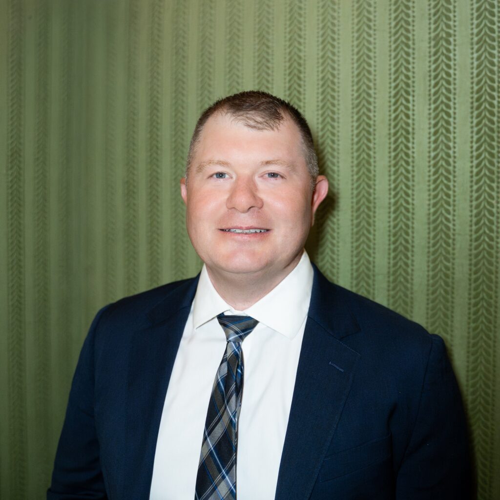 Operating Partner Mike Salzman smiles while wearing a dark suit, white shirt, and a plaid tie.