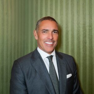 Co-founder Jorge Mora, a man in a gray suit and dark patterned tie, smiles brightly.